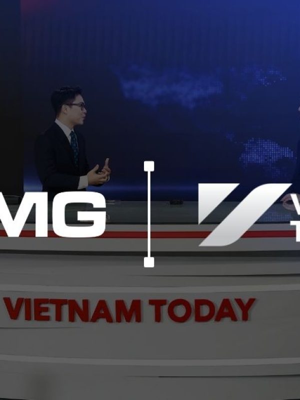 Two male news anchors sit at a circular multi-tiered desk branded 'VIETNAM TODAY' in a blue news studio with a world map backdrop and flags (South Korea and Vietnam).