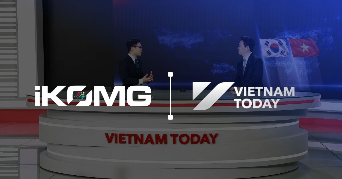 Two male news anchors sit at a circular multi-tiered desk branded 'VIETNAM TODAY' in a blue news studio with a world map backdrop and flags (South Korea and Vietnam).