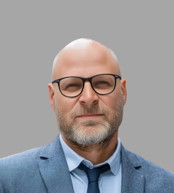 Professional head-and-shoulders portrait of a bald man with glasses in a blue suit and tie against a gray background, looking at the camera.